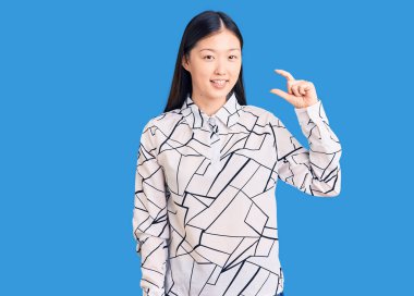 Genç, güzel, Çinli bir kadın, rahat bir tişört giyiyor, gülümsüyor, el hareketleriyle el hareketi yapıyor, parmaklarıyla işaret yapıyor ve kameraya bakıyor. ölçüm kavramı. 