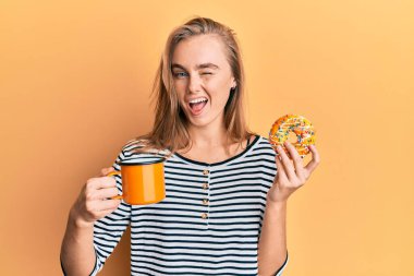 Güzel sarışın kadın donut yiyor ve kahve içiyor. Seksi bir ifadeyle kameraya bakıyor. Neşeli ve mutlu bir yüzle.. 