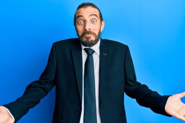 Uzun saçlı, sakallı, takım elbiseli, kravatsız, kafası karışık ve elleri havada çekici bir adam. şüphe kavramı. 