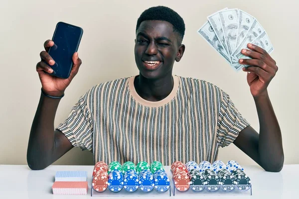 Młody Afrykański Mężczyzna Siedzący Stole Żetonami Kartami Pokerowymi Trzymającymi Smartpone — Zdjęcie stockowe