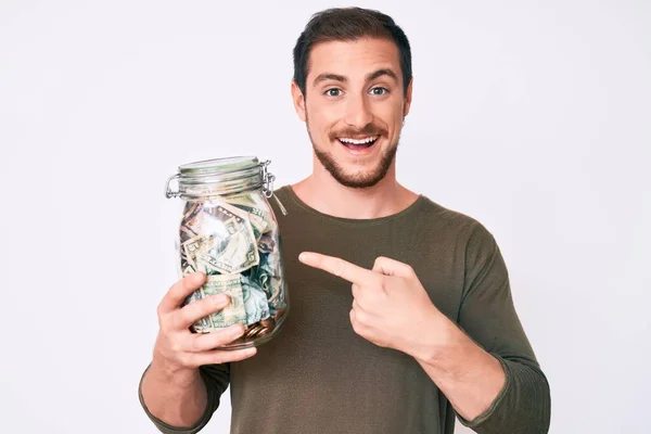 Joven Hombre Guapo Sosteniendo Frasco Con Ahorros Sonriendo Feliz Señalando — Foto de Stock