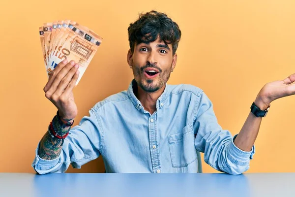 Jovem Hispânico Segurando Notas Euro Sentadas Mesa Comemorando Realização Com — Fotografia de Stock