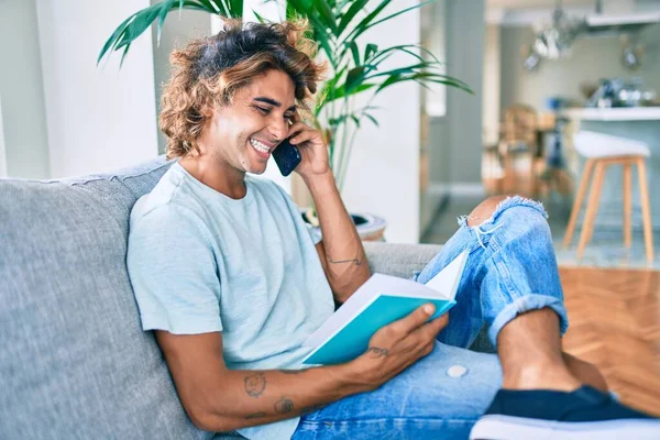 Joven Hombre Hispano Sonriendo Feliz Hablando Teléfono Inteligente Leyendo Libro —  Fotos de Stock