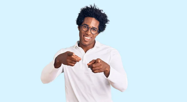 アフロの髪をしたハンサムなアフリカ系アメリカ人の男性は 陽気で面白い顔をしたカメラに指を指すカジュアルな服や眼鏡を着用しています 良いエネルギーと振動は — ストック写真