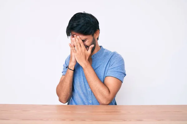 泣きながら手で顔を覆う悲しい表情でテーブルの上に座るカジュアルな服を着たハンサムなヒスパニック系の男 うつ病の概念 — ストック写真