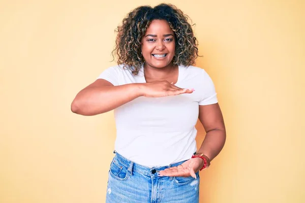 若いアフリカ系アメリカ人プラスサイズ女性を身に着けているカジュアル白いTシャツジェスチャーで手を示す大小のサイン メジャーシンボル カメラを見て笑ってる 概念を測定し — ストック写真
