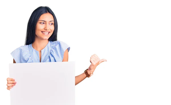 Young Beautiful Latin Girl Holding Blank Empty Banner Pointing Thumb — Stock Photo, Image