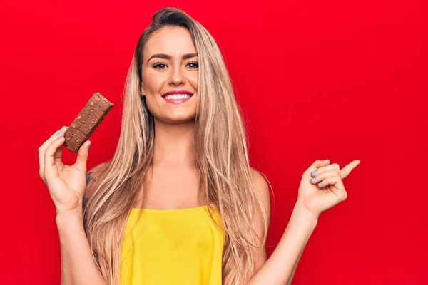 Joven Hermosa Mujer Rubia Comiendo Barra Proteína Chocolate Sobre Fondo — Foto de Stock