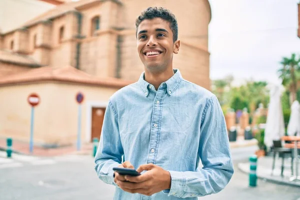 若いラテン語の男笑顔幸せな使用してスマートフォン街を歩く — ストック写真