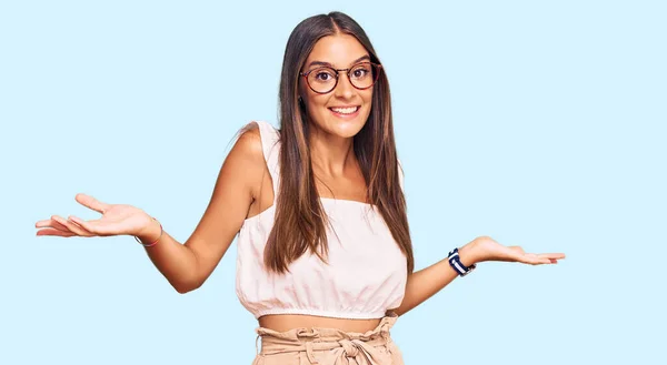 カジュアルな服と眼鏡を身に着けている若いヒスパニック系の女性は両手を開いてヤシの木を示す笑顔 提示と広告の比較とバランス — ストック写真