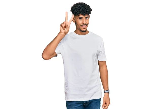 年轻的阿拉伯男子穿着休闲的白色T恤 喜形于色地微笑着 用手指在镜头前眨眼示意胜利 第二点 — 图库照片
