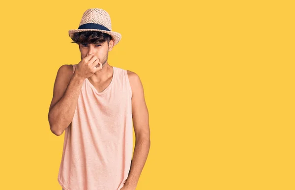 夏の帽子をかぶった若いヒスパニック系の男性は 臭いと嫌な 耐え難い匂いを嗅ぎ 鼻の上に指で息を保持しています 臭いが悪い — ストック写真