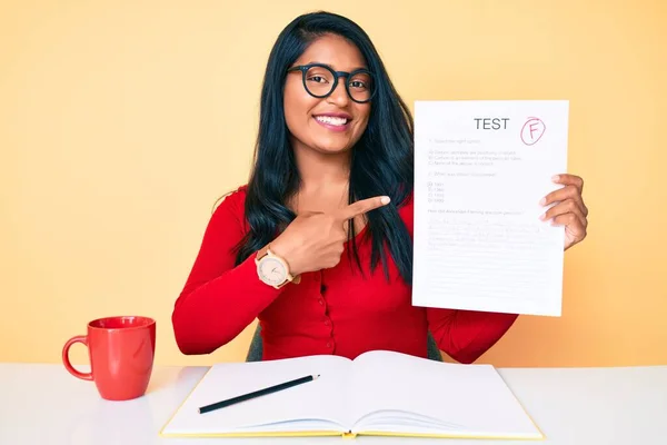 Beautiful latin young woman with long hair showing a failed exam smiling happy pointing with hand and finger