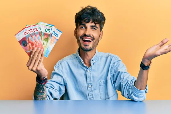 Young Hispanic Man Holding Swiss Franc Banknotes Sitting Table Celebrating — Stock Photo, Image
