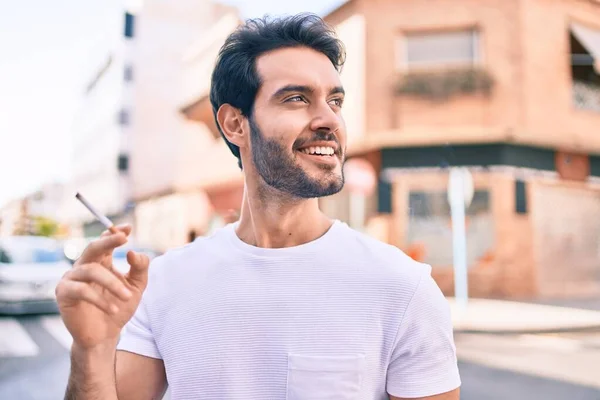 Joven Hombre Hispano Sonriendo Feliz Sosteniendo Cigarrillo Caminando Por Ciudad — Foto de Stock