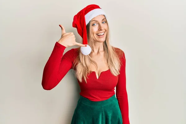 漂亮的高加索女人穿着圣诞服装 戴着帽子 微笑着用手和手指做着电话手势 就像在电话里说话一样 交流概念 — 图库照片