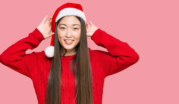 Young Chinese Woman Wearing Christmas Hat Smiling Pulling Ears Fingers — Stock Photo, Image