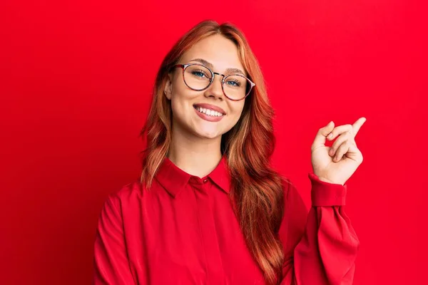 年轻美丽的红头发女人 身穿休闲装 戴着眼镜 满脸通红 手指手画脚地看着摄像机的侧面 — 图库照片