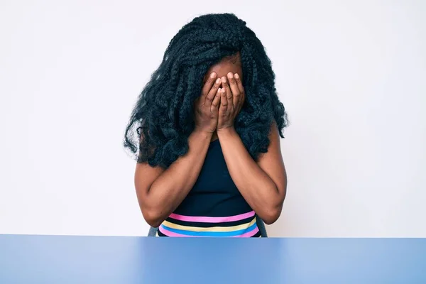 泣きながら手で顔を覆う悲しい表情でテーブルの上に座るカジュアルな服を着た美しいアフリカの女性 うつ病の概念 — ストック写真