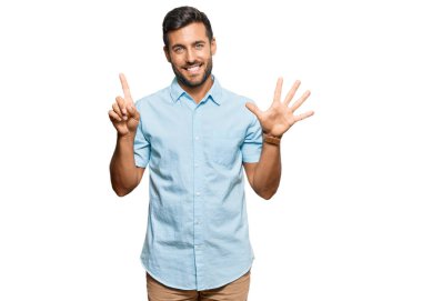 Yakışıklı İspanyol adam gündelik giysiler giyip altı numarayı gösterip işaret ederken kendinden emin ve mutlu gülümsüyor.. 