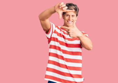 Gündelik kıyafetler giyen, gülümseyen, elleri ve parmakları gülen yüzlü genç yakışıklı bir adam. yaratıcılık ve fotoğrafçılık kavramı. 