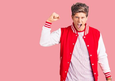 Beyzbol üniforması giyen genç ve yakışıklı bir adam öfkeyle bağırırken sinirli ve öfkeli bir şekilde yumruk kaldırıyor. öfke ve agresif konsept. 