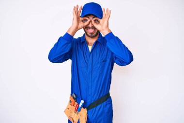 Kıvırcık saçlı ve ayı gibi giyinen yakışıklı genç adam. Dürbün gibi jest yapıyor. Gözleri parmaklarından bakıyor. çılgın ifade. 