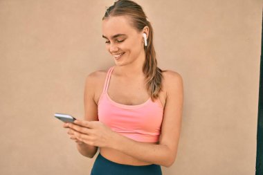 Genç sarışın sporcu şehirde akıllı telefon kullanarak egzersiz yapıyor..