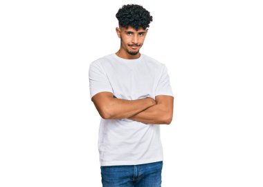 Gündelik beyaz tişört giyen, kuşkucu ve gergin genç bir Arap. Yüzünde çapraz kollu tasvip etmeyen bir ifade var. negatif kişi. 