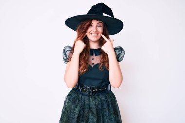 Cadılar bayramı kostümü giymiş genç ve güzel bir kadın ağzı açık gülümsüyor, parmakları işaret ediyor ve neşeli bir gülümseme sergiliyor. 