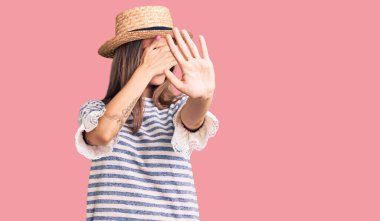 Yazlık şapkalı güzel beyaz kadın elleriyle gözlerini kapatıyor ve üzgün ve korku ifadeleriyle jest yapıyor. utangaç ve olumsuz kavram. 