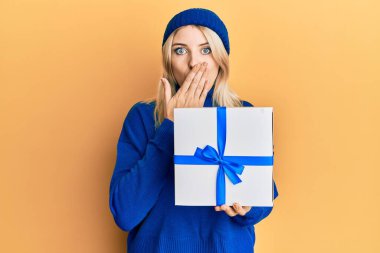 Genç, beyaz bir kadın elinde hediyeyle ağzını eliyle kapatıyor. Şok olmuş ve hata yapmaktan korkuyor. şaşırmış ifade 