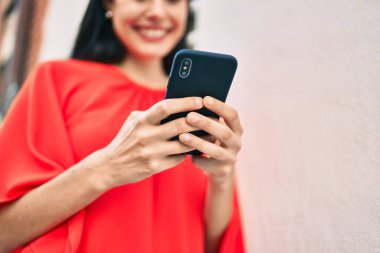 Genç Latin kız şehirde akıllı telefon kullanarak mutlu bir şekilde gülümsüyor..