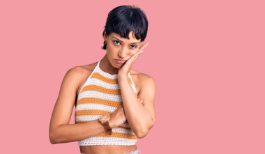 Kısa saçlı genç esmer kadın gündelik kıyafetler giyip kollarını kavuşturarak depresyondan sıkılmış ve yorgun görünüyor.. 