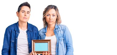 Boş çerçeve tutan bir çift kadın ciddi bir ifadeyle gevşemiş. Basit ve doğal bir şekilde kameraya bakıyorsun.. 