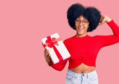 Genç Afrikalı Amerikalı kız elinde hediyeyle çılgın ve elleri başında korkmuş, korkmuş ve ağzı açık şoktan şaşırmış. 
