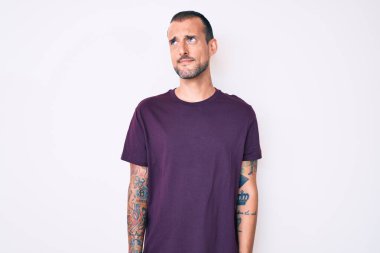 Dövmeli genç, yakışıklı, sıradan kıyafetler giyen, gülümseyen, yan tarafa bakan ve düşünen bir adam.. 