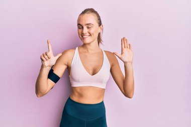 Spor giyim ve kol bandı takan güzel sarışın kadın yedi numaralı parmaklarını gösterip işaret ederken kendine güvenen ve mutlu bir şekilde gülümsüyor.. 