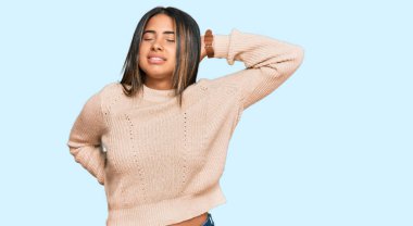 Kışın yün kazak giyen, boynu ağrıyan, eli boynuna dokunan, kas ağrısı çeken genç bir Latin kız. 