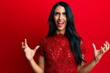Güzel İspanyol bir kadın kırmızı arka planda şık kıyafetler giyip deli gibi bağırıyor ve agresif bir ifade ve kollarla bağırıyor. hüsran kavramı. 