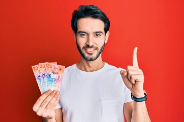 İspanyol asıllı genç adam elinde İsviçre frangı banknotları tutarken bir fikir veya soruyla gülümsüyor ve mutlu bir yüzle işaret ediyor. 