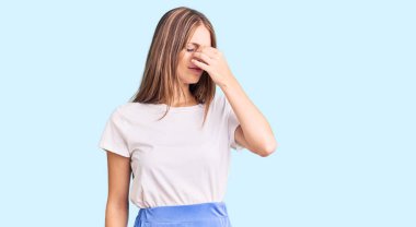 Genç, sarışın, yaz tarzı giyinen, burnu ve gözleri ovuşturmaktan yorgun, yorgun ve baş ağrısı çeken bir kadın. Stres ve hüsran kavramı. 