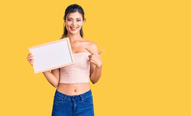 Elinde boş beyaz karatahta tutan genç ve güzel bir kadın gülümsüyor. 