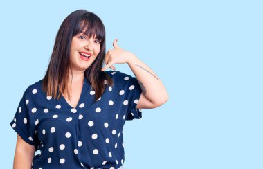 Genç ve cüsseli bir kadın günlük kıyafetler giyiyor gülümsüyor telefonla el ve parmaklarıyla jest yapıyor telefonda konuşuyor gibi. iletişim kavramları. 