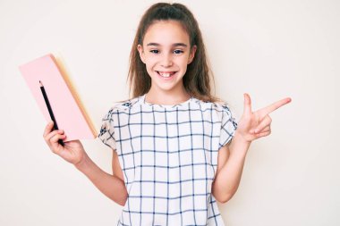 Sevimli İspanyol çocuk, elinde kitap ve kalemle gülümsüyor, mutlu bir şekilde elini ve parmağını yana uzatıyordu. 