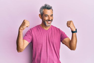 Orta yaşlı, gri saçlı, günlük kıyafetler giymiş gururla bağıran, zaferi kutlayan ve kollarını kaldırarak heyecanlanan bir adam. 