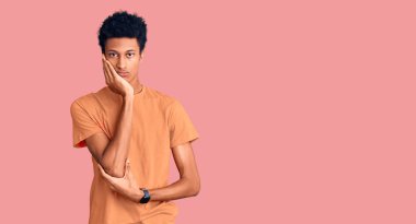 Genç, Afro-Amerikalı bir adam günlük kıyafetler giyip kollarını kavuşturup depresyondan sıkılmış ve yorgun görünüyor.. 