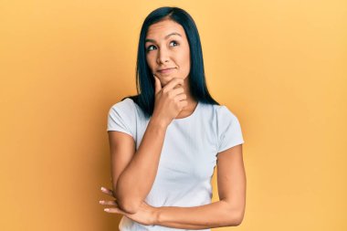 Güzel İspanyol kadın, elleri çenesinde, gündelik beyaz tişört giyip soru soran, düşünceli bir ifade takınıyor. Düşünceli bir yüzle gülümsüyor. şüphe kavramı. 