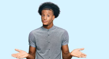 Afro saçlı, sıradan kıyafetler giyen, elleri ve kolları havada, kafası karışmış Afro-Amerikan bir adam. şüphe kavramı. 