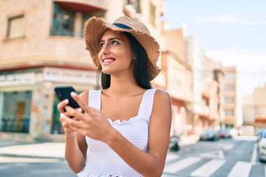 Yaz tarzı giyinen genç Latin kız şehrin caddesinde akıllı telefon kullanıyor..
